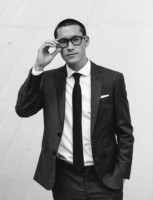 Image of Perry in black and white wearing a custom Brooklyn Tailors suit. He is adjusting his glasses. 