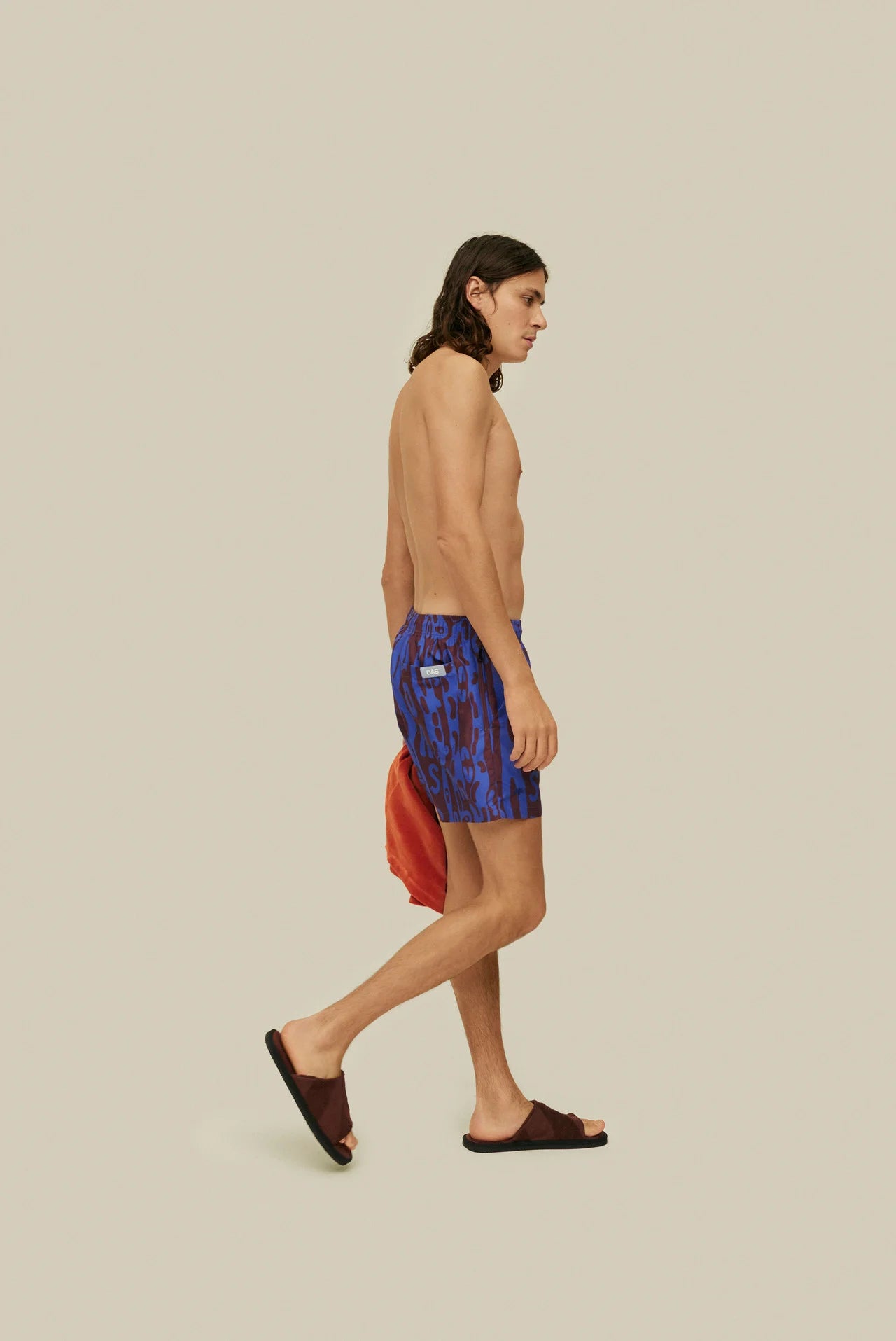 OAS Thenards Jiggle Swim Shorts on model. Model is wearing swim shorts carrying orange terry shirt. Taken from side.