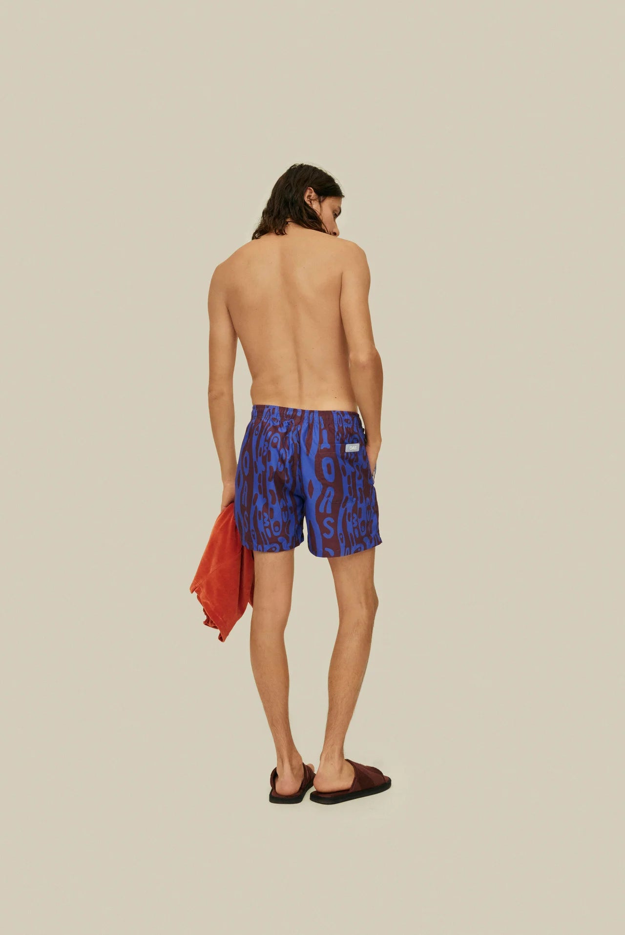 OAS Thenards Jiggle Swim Shorts on model. Model is wearing swim shorts carrying orange terry shirt. Taken from back.