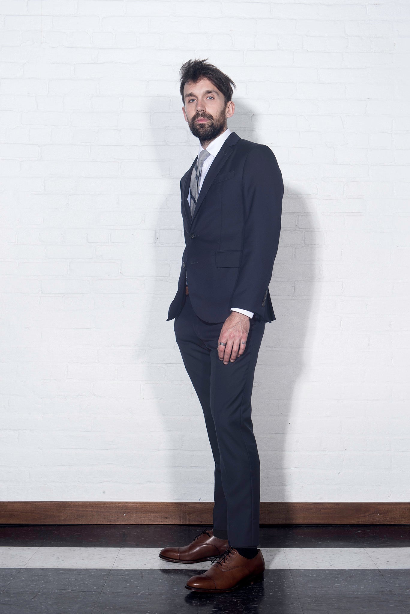 Brooklyn tailors BKT50 Tailored Jacket in Super 110s Plainweave - Classic Navy on-body shot from the side. Model is wearing the jacket with matching pants, a white dress shirt and gray striped tie.