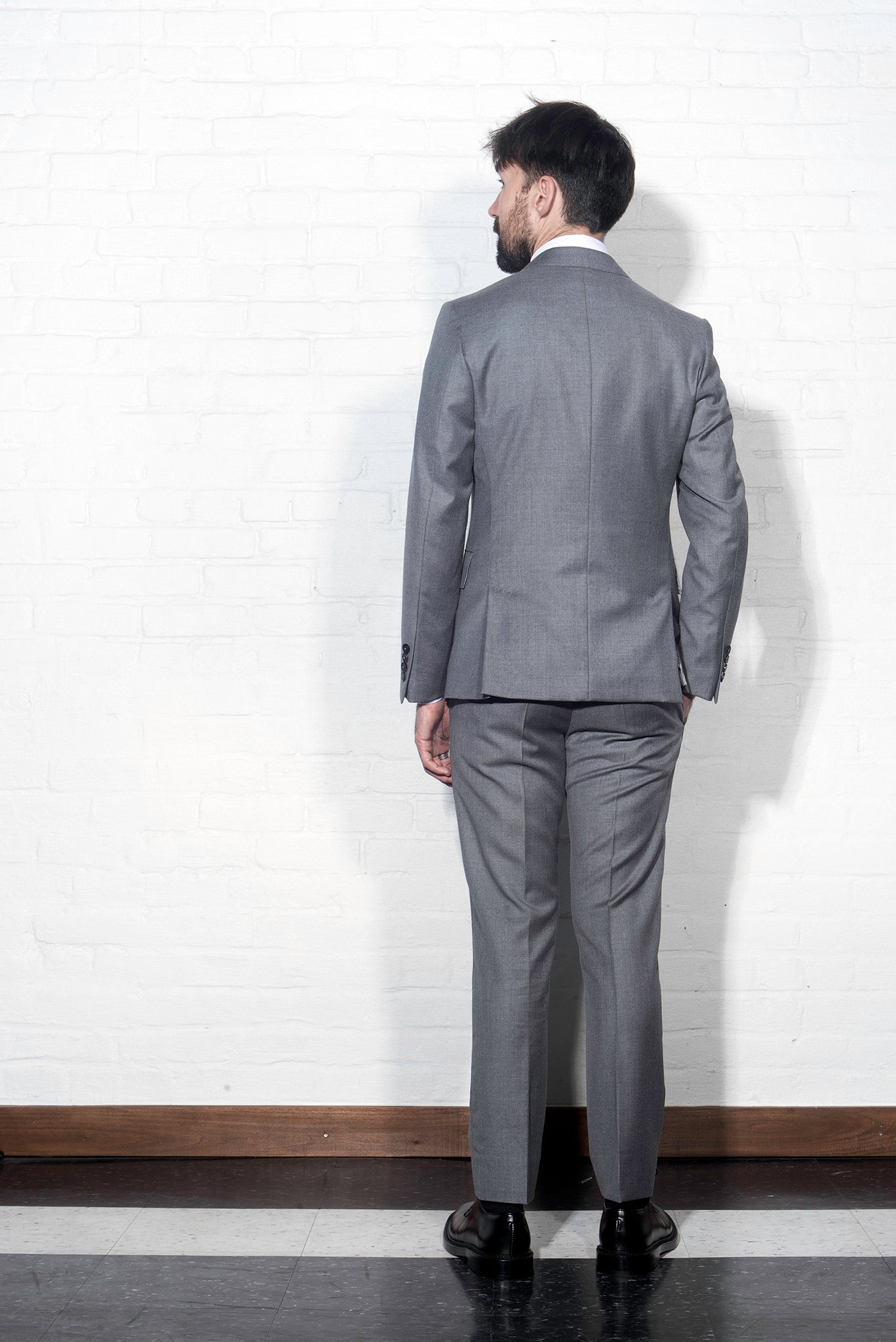 Brooklyn Tailors BKT50 Tailored Jacket in Super 110s Twill - Dove Gray on-body shot from the back. Model is wearing jacket with matching pants, white dress shirt, tie, and black belt. 