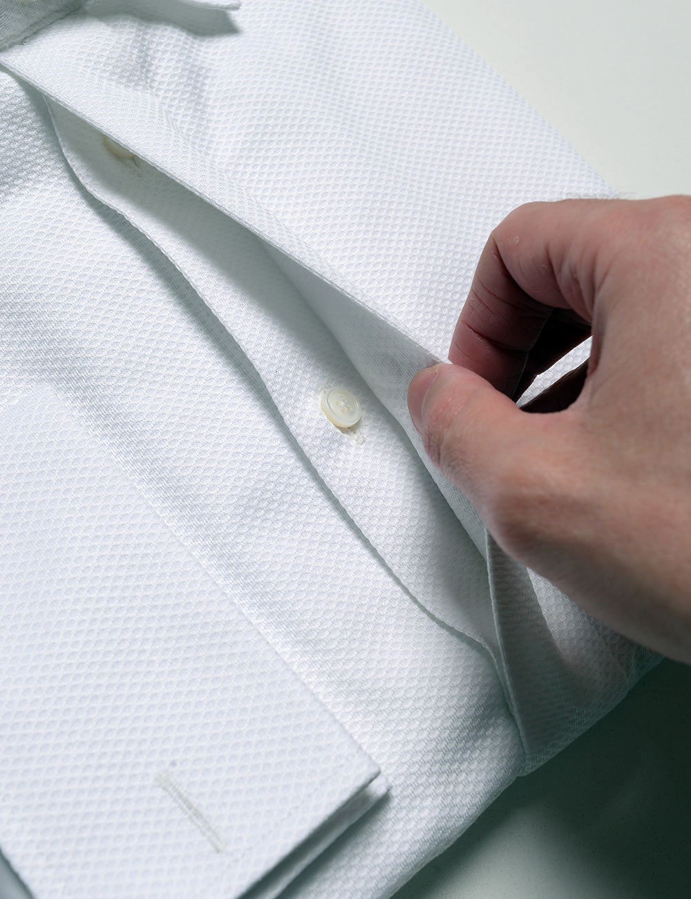 Detail shot showing a hand moving the covered placket to reveal the buttons underneath on Brooklyn Tailors BKT20 Classic French Cuff Tuxedo Shirt - Waffle Pique