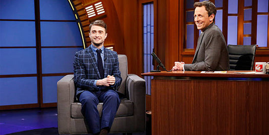 Daniel Radcliffe sits next to Seth Myers wearing a Brooklyn Tailors navy plaid suit
