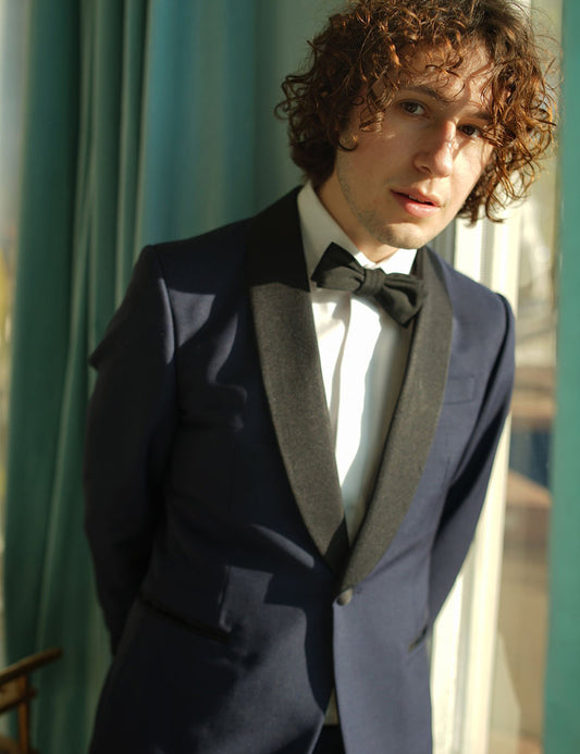 Model wears navy tuxedo jacket with white tux shirt and black bow tie. 