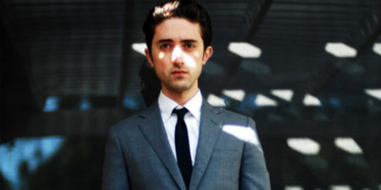 Daniel wears a charcoal suit with light streaming across his face and backdrop