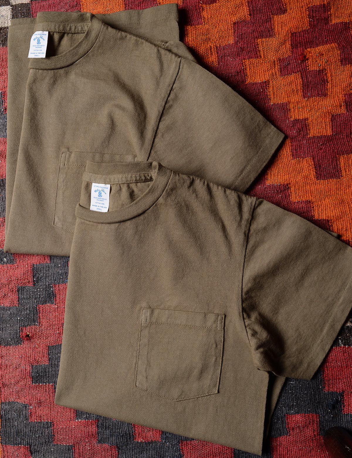 Photo of folded Velva Sheen 2-Pack Short Sleeve Pocket Tee in Olive on a colorful rug