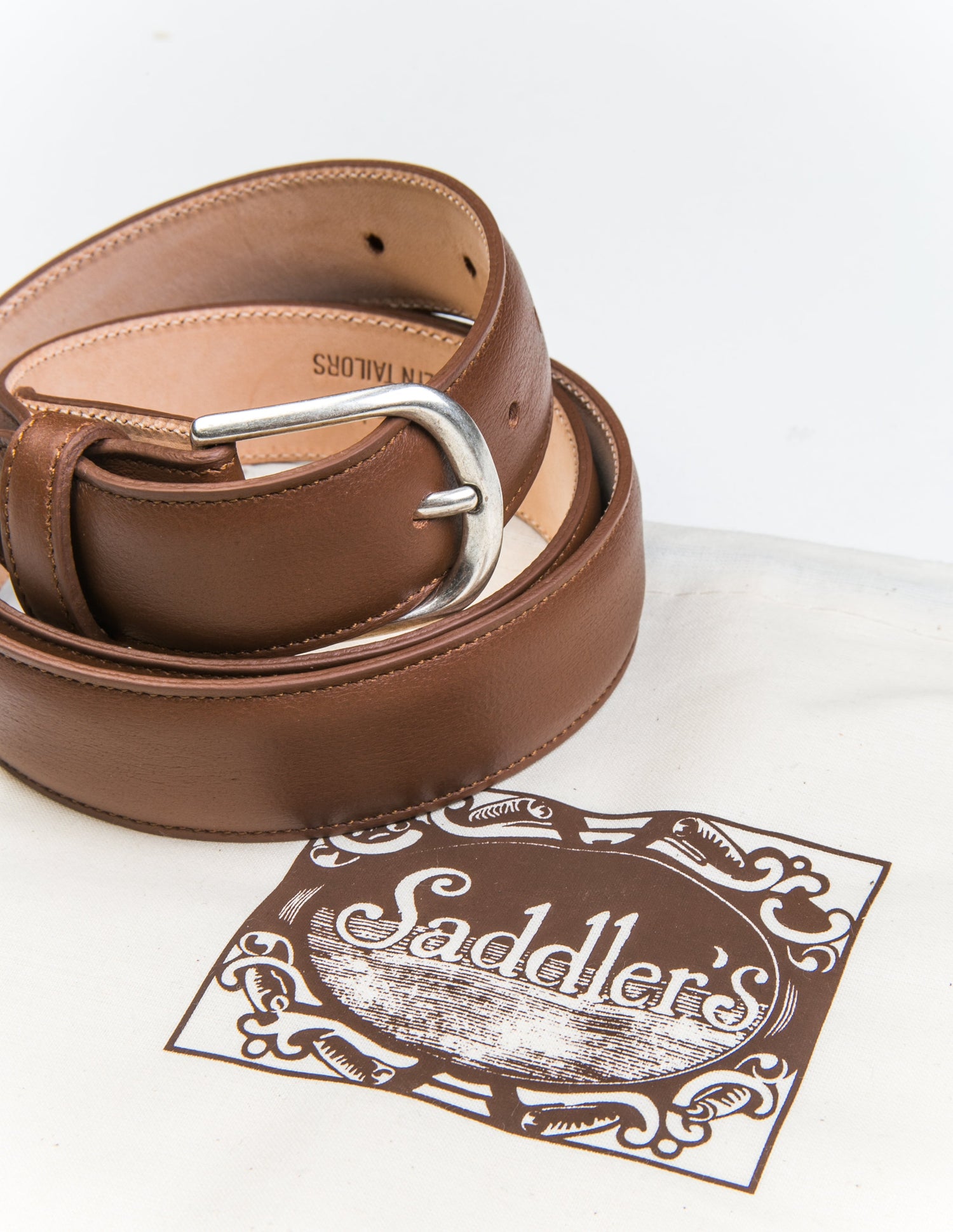 Brooklyn Tailors x Saddler's 30mm Belt in Smooth Leather - Honey Brown coiled next to the fabric dust bag it's sold with. 