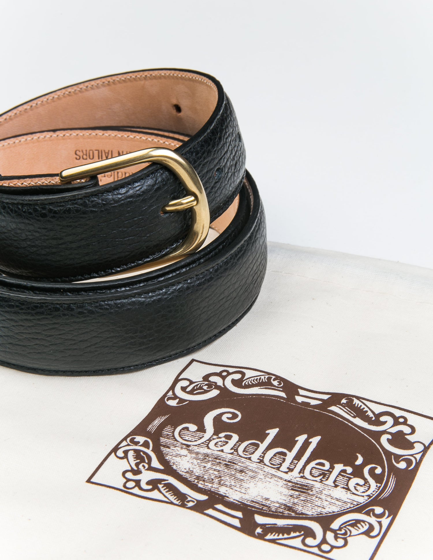 Photo of Brooklyn Tailors x Saddler's 30mm Belt in Grain Leather - Black coiled next to the fabric bag it's sold with. 