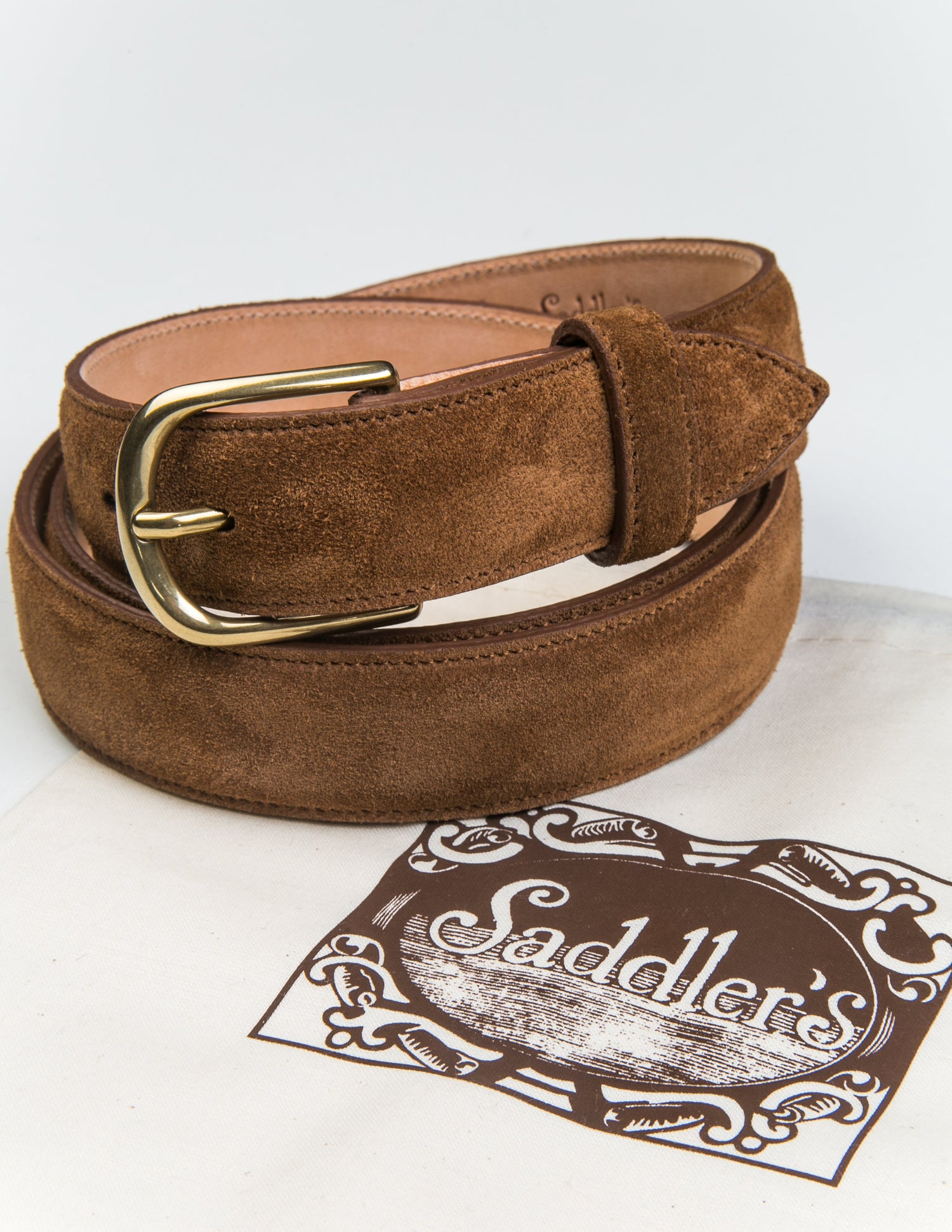 Brooklyn Tailors x Saddler's 30mm Belt in Suede Leather - Warm Brown coiled next to the fabric dust bag it is sold with. 