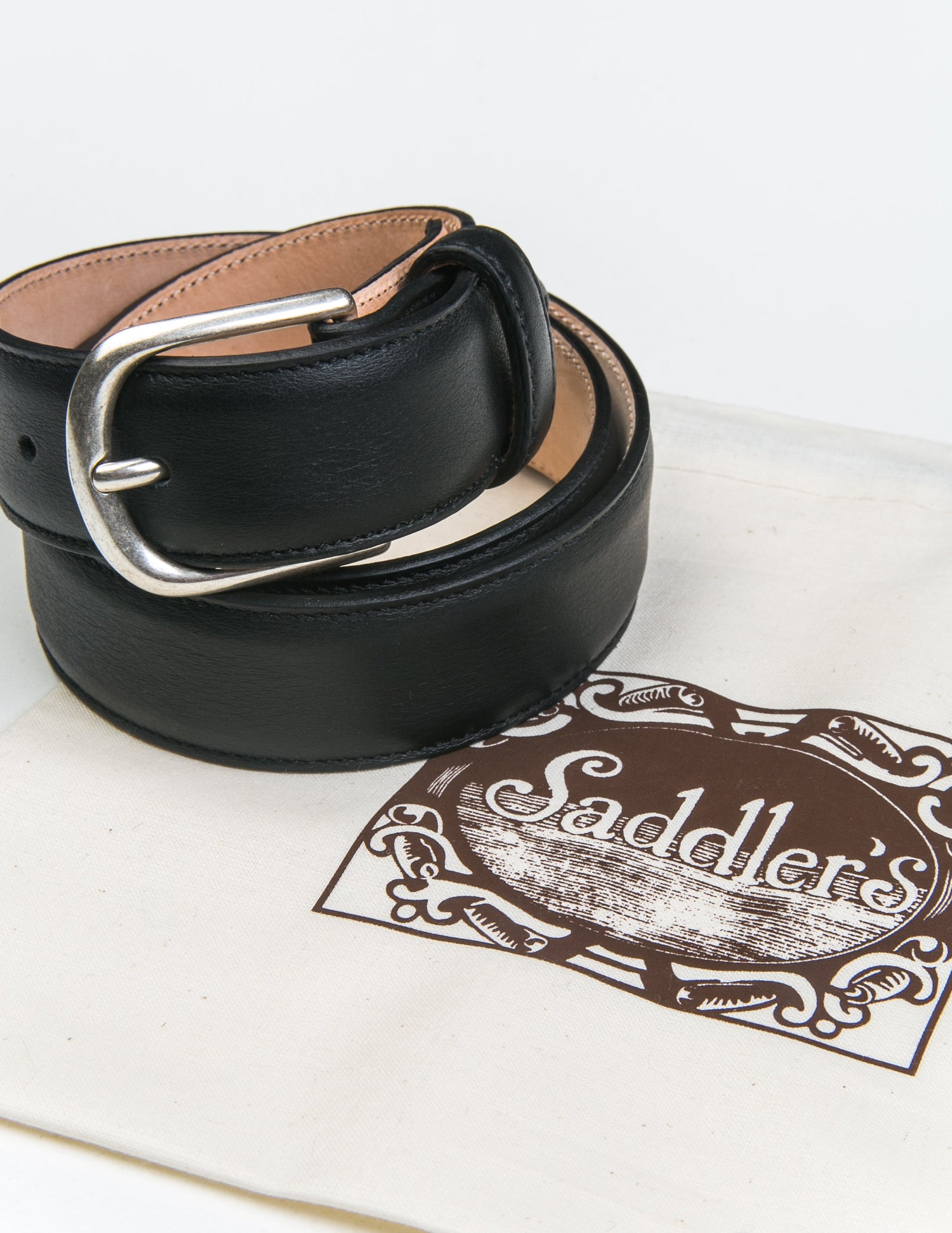 Photo of Brooklyn Tailors x Saddler's 30mm Belt in Smooth Leather - Black coiled next to the fabric bag it is sold with. 