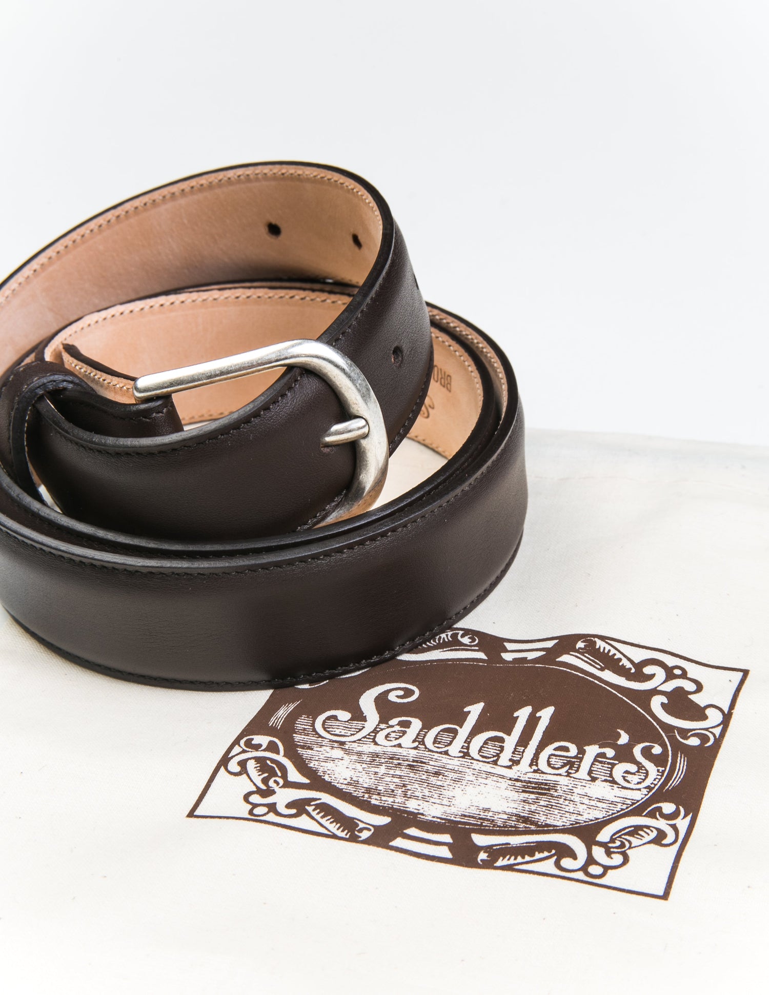 Photo of Brooklyn Tailors x Saddler's 30mm Belt in Smooth Leather - Cacao coiled next to the fabric bag it's sold with