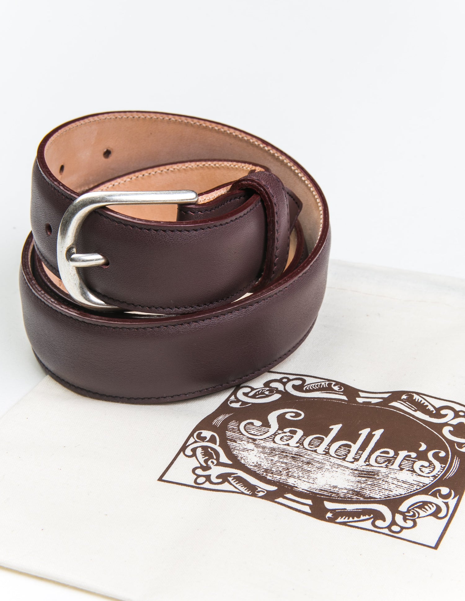 Photo of Brooklyn Tailors x Saddler's 30mm Belt in Smooth Leather - Bordo coiled next to the fabric bag it's sold with. 
