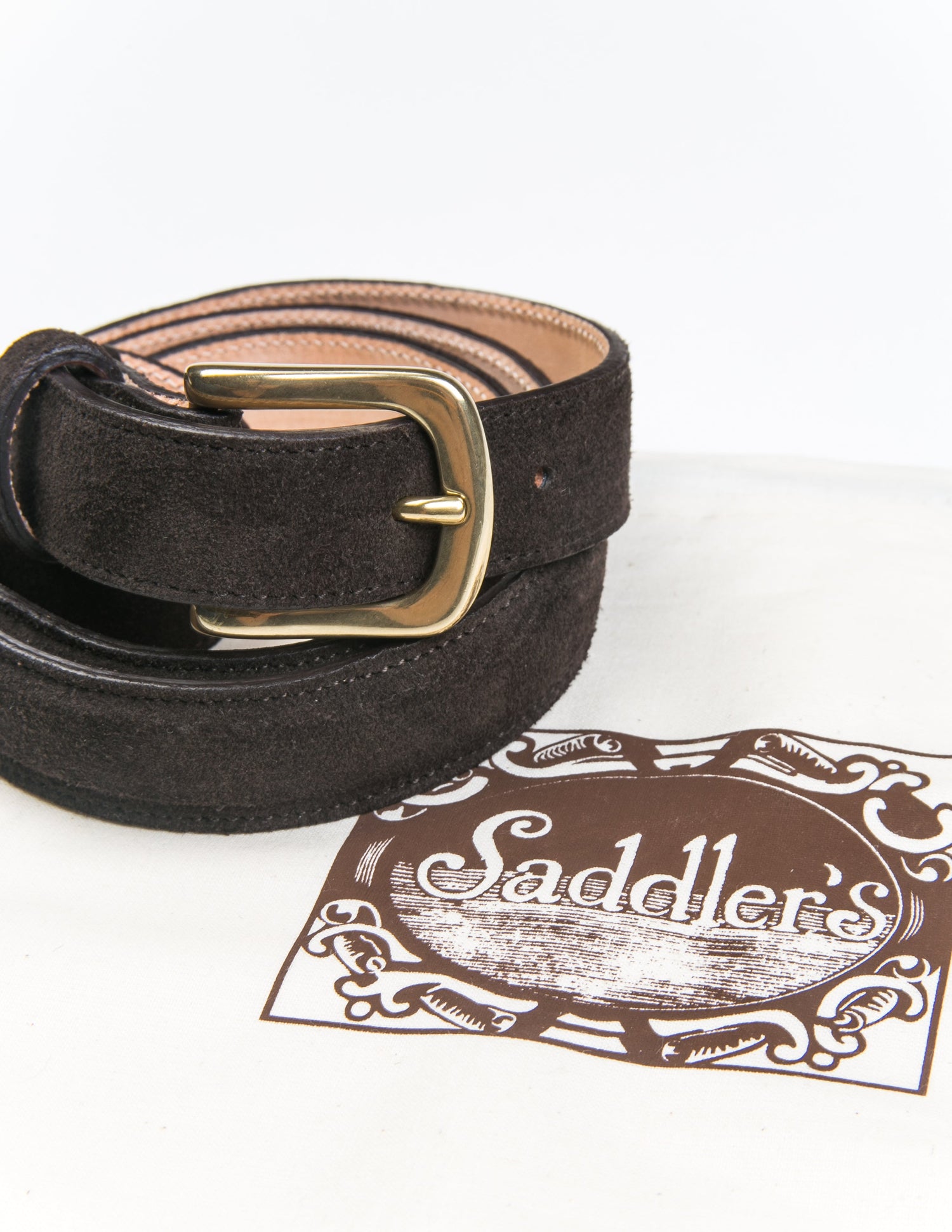 Photo of Brooklyn Tailors x Saddler's 25mm Belt in Suede Leather - Deep Brown coiled next to the fabric bag it is sold with. 
