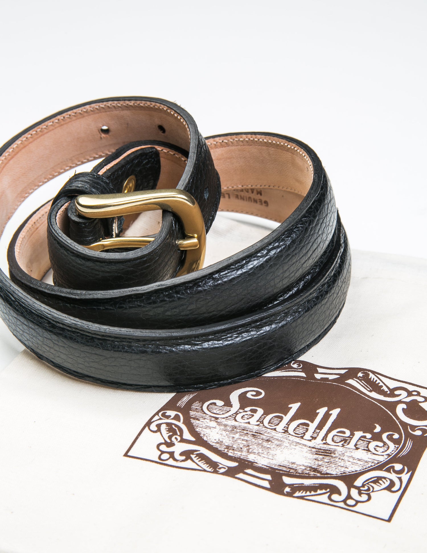 Photo of Brooklyn Tailors x Saddler's 25mm Belt in Grain Leather - Black coiled next to the fabric Saddler's bag that the belt is sold with.