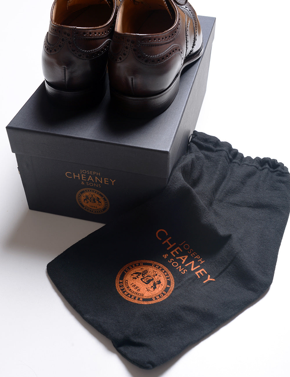 Photo of Joseph Cheaney Arthur III Oxford Brogue  in Mocha Calf Leather on top of their box next to the branded dust bag the shoes are sold with. 