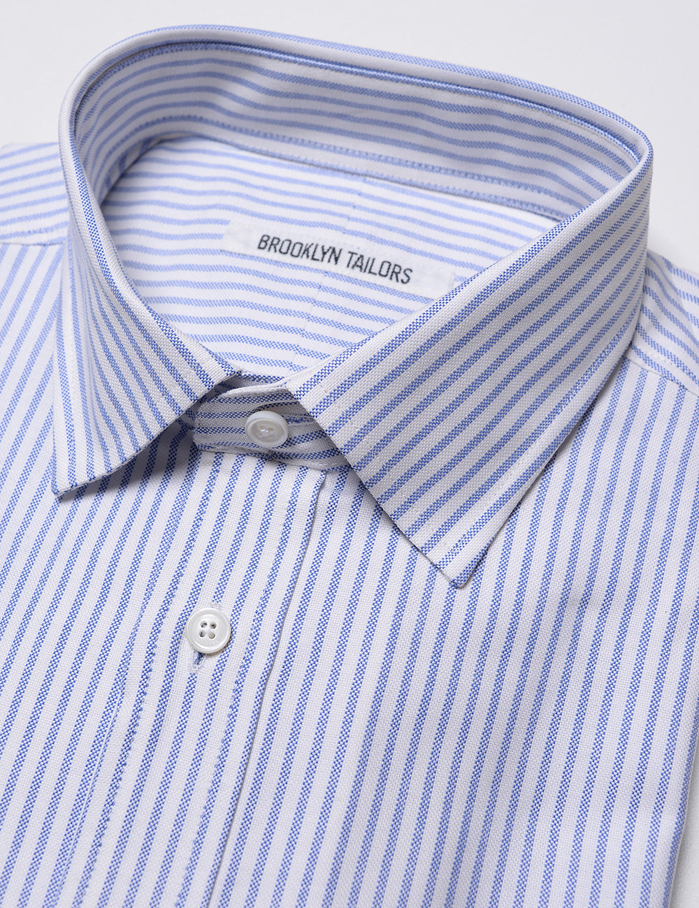 Detail of collar, labeling, buttons, and fabric pattern and texture on Brooklyn Tailors BKT20 Slim Dress Shirt in Striped Oxford - White / Sky Blue