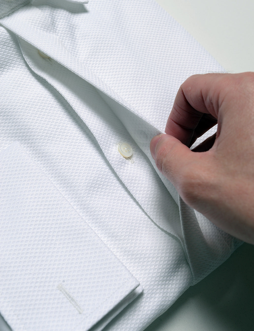 Detail shot showing a hand moving the covered placket to reveal the buttons underneath on Brooklyn Tailors BKT20 Classic French Cuff Tuxedo Shirt -  Waffle Pique
